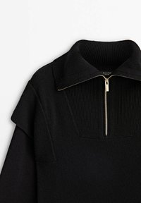 Pull à côtes noirs avec un large col et une demi-fermeture éclair dorée à l'avant, présenté sur un fond blanc.