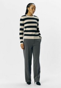Schwarz-beige gestreifter Strickpullover mit geripptem Muster, kombiniert mit grauen maßgeschneiderten Hosen und schwarzen spitz zulaufenden Heels.
