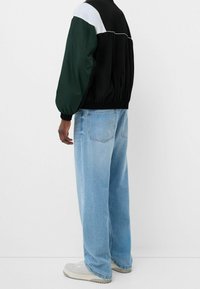 Färgglad jacka med svart, grön och vit tyg, elastisk midja; matchad med ljusblå vida jeans i texturerat denimtyg.