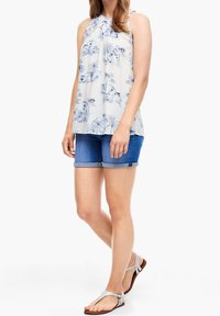 Lichtblauw haltertop met bloemenprint en een losse pasvorm; gecombineerd met denim shorts. Beige sandalen maken de outfit compleet. Gladde stof met een subtiele textuur.