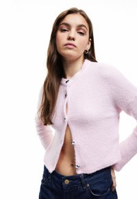 Cardigan a maglia rosa chiaro con texture a coste, scollatura rotonda e chiusure con bottoni argentati. Presenta una vestibilità cropped e maniche lunghe.