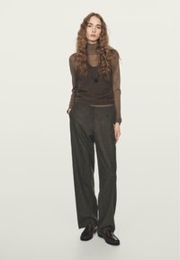 Brown turtleneck sweater layered under a sleeveless brown vest, paired with charcoal gray, tailored wide-leg trousers and dark shoes.