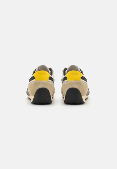 Black and gray sneakers with beige suede accents and yellow heel tabs. Features textured rubber soles and a modern design.