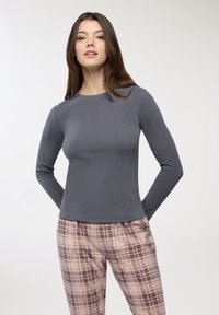 Maglia grigia a maniche lunghe con scollo rotondo e texture a coste, abbinata a pantaloni a fantasia tartan chiara in colori tenui.