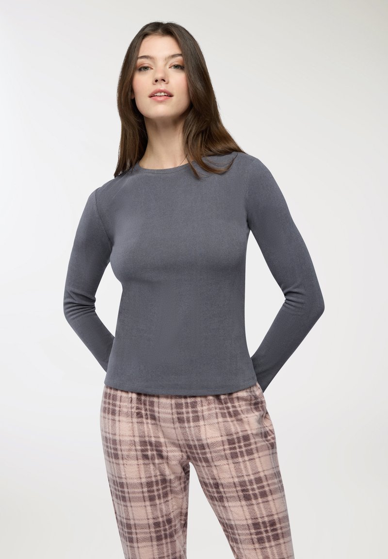 Maglia grigia a maniche lunghe con scollo rotondo e texture a coste, abbinata a pantaloni a fantasia tartan chiara in colori tenui.