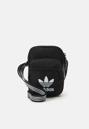 Mustmust värvi risti koti, millel on tõmblukuga sulgemine, valge Adidas'i logo ja triibuline reguleeritav rihm mugavaks kandmiseks.