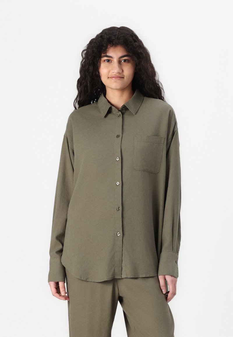 Camisa verde-oliva com botões, com colarinho pontudo, mangas longas e um único bolso no peito. Feita de um tecido leve e macio.
