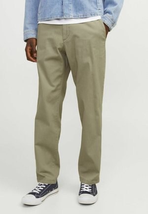 Chinos en kaki avec une coupe droite, fabriqués en coton. Présente une texture lisse, des poches avant et sont portés avec des baskets navy.