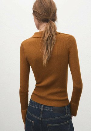 Suéter marrón acanalado con cuello de solapa, mangas largas y diseño ajustado, combinado con jeans de mezclilla oscura y costuras visibles.