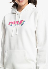 Witte hoodie met een kleurraf"roxy" grafisch ontwerp op de borst. Het heeft een buidelzak en koorden aan de capuchon. Zachte textuur.