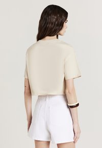 Beige T-Shirt, kurzärmlig, glattes Material, kombiniert mit weißen, hochtaillierten Shorts mit Gesäßtaschen und einem strukturierten Armband.