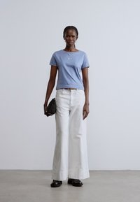 Tricou albastru deschis cu un mic detaliu brodat, asortat cu pantaloni largi albi, pantofi negri și o geantă mică neagră. Design minimalist.