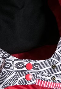 Gros plan sur un tissu à motif noir et blanc avec deux boutons-pression rouges et deux boutons-pression métalliques ouverts sur fond rouge.
