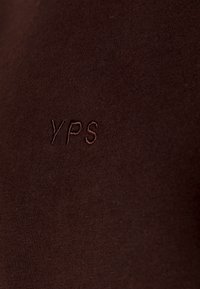 Brauner Baumwollstoff mit gestickten Initialen "YPS" in einem passenden Farbton, mit glatter Textur und minimalistischem Design.