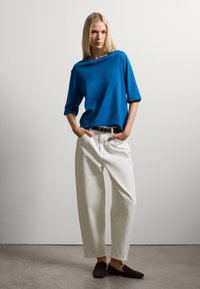 Top azul de manga corta con escote barco, combinado con pantalones blancos de pierna ancha y zapatos oscuros tipo slip-on. Diseño sencillo, sin patrones ni acentos.