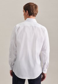 Camicia bianca a maniche lunghe con colletto classico, polsini abbottonati e orlo curvo. Tessuto liscio e design sobrio.