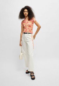 Short-sleeve, tie-dye top in pink and orange hues, featuring ruching at the side, paired with high-waisted white pants and black platform sandals.