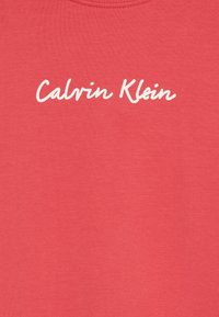 Rød bomull T-skjorte med en hvit kursiv "Calvin Klein"-logo over brystet. Glatt tekstur og rund halsutringning.