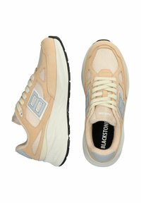 Beige athletic sneakers with mesh and suede materials, featuring a cream midsole, gray accents, and lace-up closure. Durable black rubber outsole.