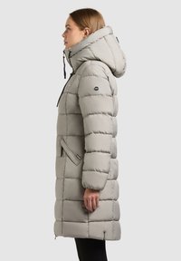 Ljusgrå pufferjacka med huva, med en quiltad design, framdragkedja och två sidofickor. Slät, vadderad textur.