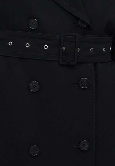 Μαύρο παλτό διπλής σειράς με ζώνη από το ίδιο ύφασμα με μεταλλικές τρύπες και ορθογώνια αγκράφα, δεμένη γύρω από τη μέση.