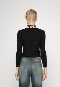 Schwarzes, geripptes Langarmoberteil mit einem Krawatten-Ausschnitt, kombiniert mit blauen Jeans aus Denim, die sichtbare Gesäßtaschen und eine helle Wäsche aufweisen.