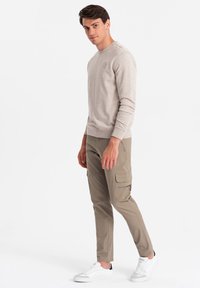 Felpa beige chiaro con scollatura a girocollo e dettaglio del logo, abbinata a pantaloni cargo grigi chiari con tasche con zip e sneakers bianche.