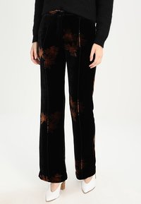 Zwarte fluwelen broek met bruine bloemenpatronen, rechte pijpen, een textuurstof en een op maat gemaakte tailleband. Gestyled met witte hakken.