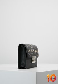 Black faux leather handbag with a textured surface, embellished with gold studs on the flap, featuring a silver clasp closure.