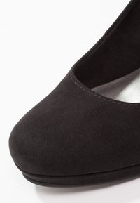 Escarpin en daim noir avec un bout rond, doublure intérieure lisse et une couture subtile le long du bord. Sa forme est élégante et raffinée.
