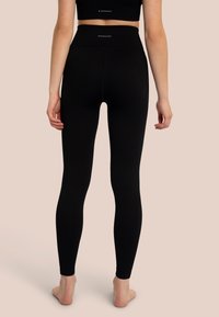 Leggings neri a costine con vita alta. Il tessuto sembra elastico, con una texture liscia e un marchio discreto sulla cintura.