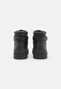 Zapatillas negras de tobillo bajo hechas de cuero liso. Presentan un cuello acolchado, suela plana y un diseño minimalista sin logotipos visibles.