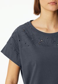Grijze T-shirt met korte mouwen, voorzien van een geborduurd bloemenpatroon op de schouders, met uitsnijdingen en een ronde halslijn.