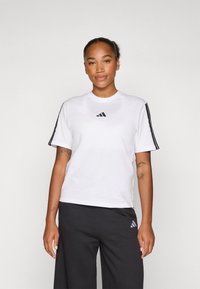Bela kratka majica s kratkimi rokavi iz zračnega materiala, ki na prsih vsebuje črni Adidas logo in črne črte na rokavih.