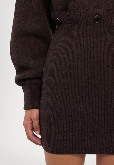 Brun ribbet sweaterkjole med en tætsiddende talje, der har to synlige sorte knapper ved taljelinjen og let puffede ærmer.