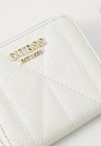 Weißer texturierter Geldbeutel mit sich wiederholendem Muster, goldenem Logo "GUESS EST 1981" und subtilen Nähdetails auf der Außenseite.