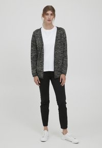 Gray and black knit cardigan with an open front, worn over a white t-shirt, paired with black pants and white sneakers. Simple, textured design.