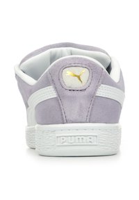 Sneakers Puma con tomaia in suede lavanda, accenti bianchi, suola in gomma bianca testurizzata e una etichetta logo dorata sul tallone.