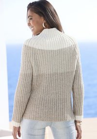 Strickpullover mit gerippter Textur, in hellbeige und cremigen Farben, mit hohem Kragen und langen Ärmeln, kombiniert mit hellen Jeans.