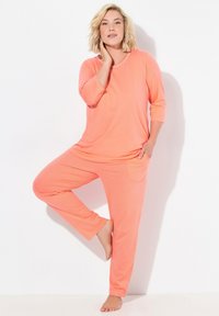 Korallfärgad loungewear-set med topp med 3/4 ärm och prickiga byxor. Mjuk tyg, avslappnad passform, framfickdetalj på byxorna.