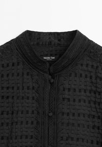 Black textured jacket with embroidered floral details and fabric-covered buttons, featuring a round collar and grid pattern fabric.