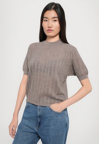 Krátky rukáv, svetlohnedý pletený top s vertikálnou rebrovanou textúrou a okrúhlym výstrihom, skombinovaný so stredne modrými džínami s vysokým pásom.