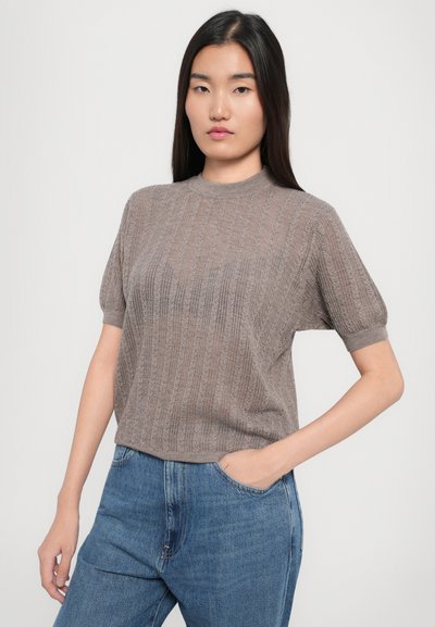 Maglietta a maniche corte di colore marrone chiaro in maglia con texture a coste verticali e scollatura a girocollo, abbinata a jeans a vita alta di blu medio.