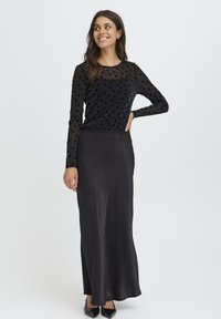 Sort langærmet bluse med teksturerede prikker, parret med en flydende sort satin maxi-nederdel. Sorte flade sko fuldender outfittet.