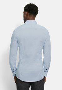 Blaue Hemd mit kleinem Punkte-Muster, langen Ärmeln und klassischem Kragen. Mit Knopfmanschetten und taillierter Passform.