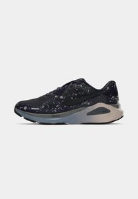 Zapatilla deportiva negra con un patrón moteado, material suave, punta redondeada y mediasuela acolchada; presenta un logo de Nike en negro.