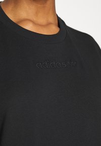 T-shirt in cotone nero con colletto a girocollo a costine e logo ricamato "adidas" in tono sul petto, che mostra una superficie liscia.