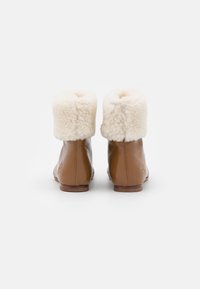 Bottines en cuir marron avec un revers en fausse fourrure, forme arrondie et texture lisse. Elles présentent un talon plat et des détails de couture subtils.