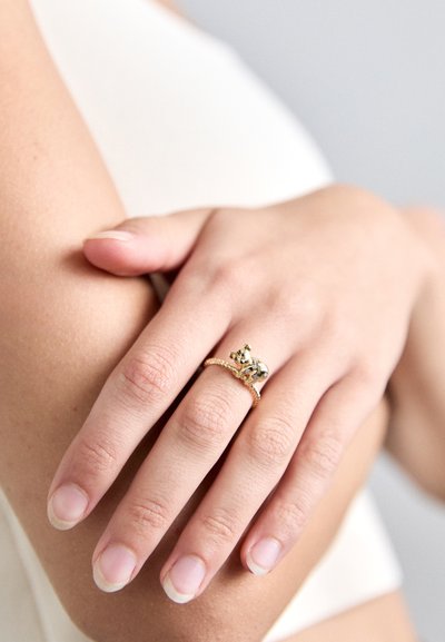 Κοντινός πλανός ενός χεριού που φορά ένα χρυσό δαχτυλίδι σε σχήμα κοάλα που αγκαλιάζει το δάχτυλο, με φυσικά νύχια και ανοιχτόχρωμο τόνο δέρματος.