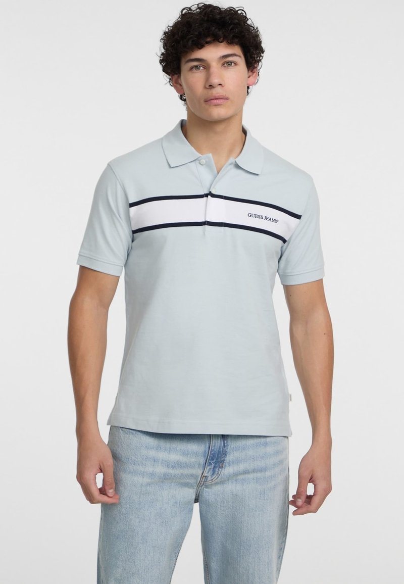 Polo de color azul claro, hecho de algodón, con mangas cortas, que presenta una banda a rayas blanca y azul marino y un logotipo en el pecho. Corte relajado.
